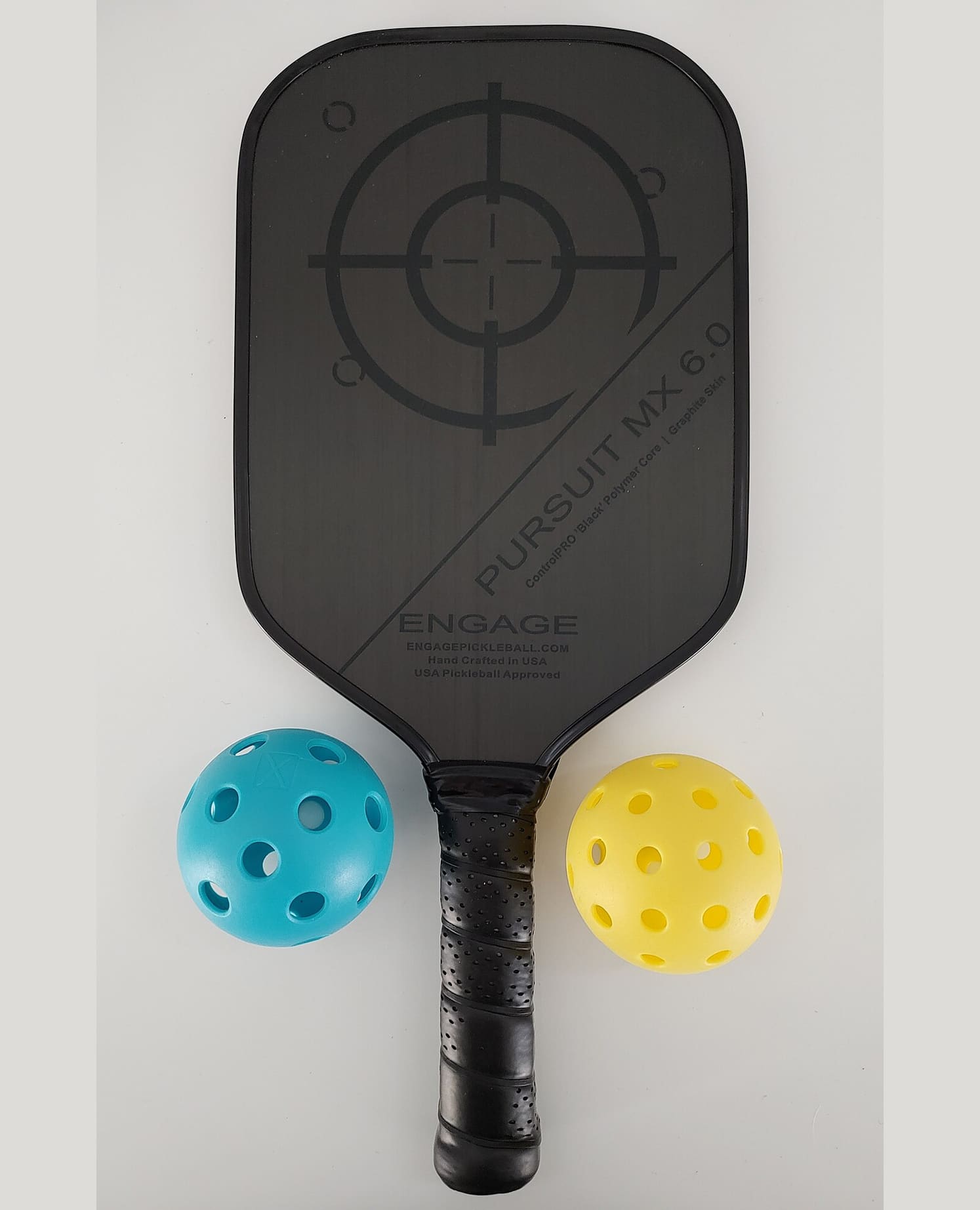 A pickleball paddle with two balls beside it: a blue indoor ball with larger holes and a yellow outdoor ball with smaller ones.