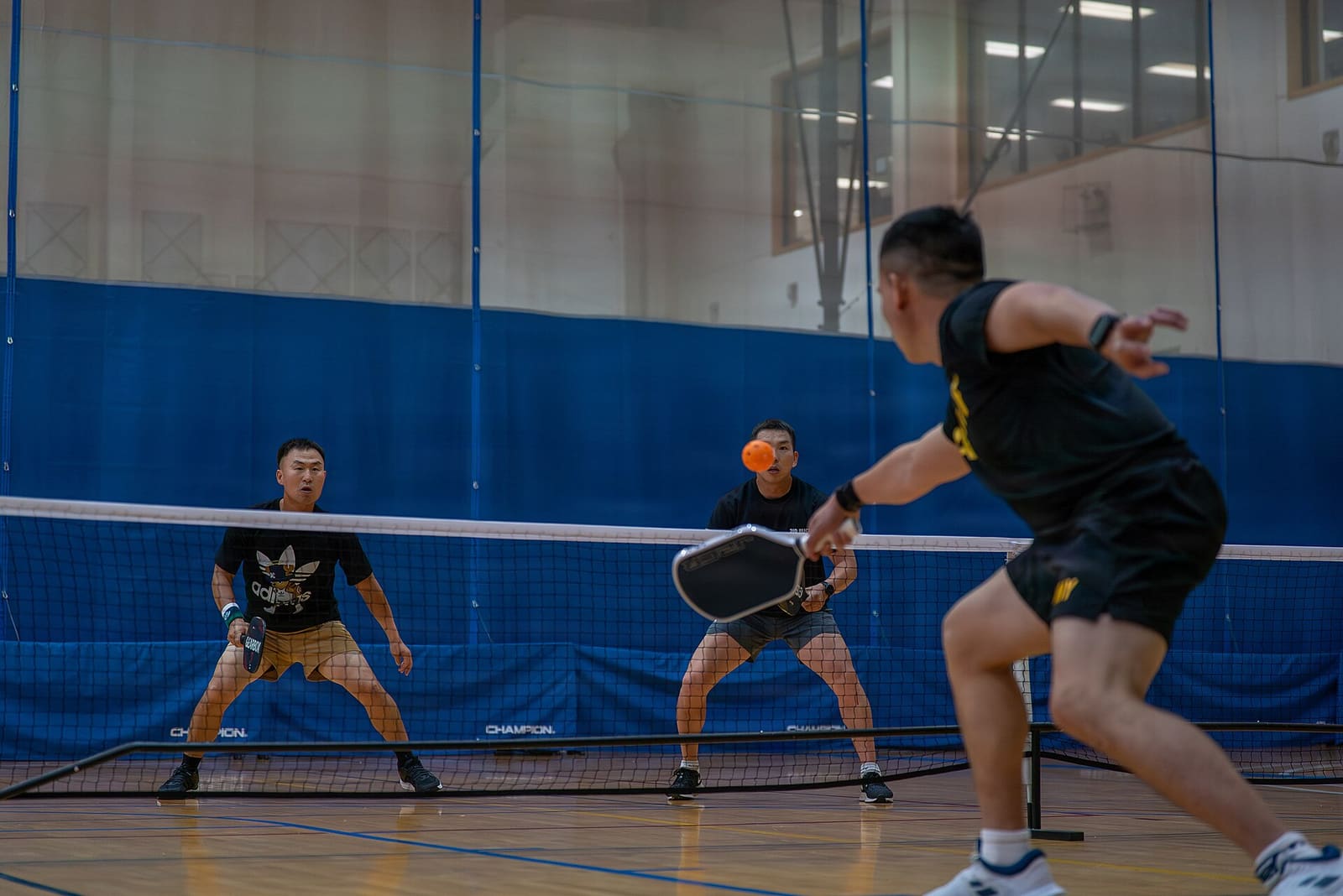 Two players crouched in ready position at the net as a hard shot comes toward them.