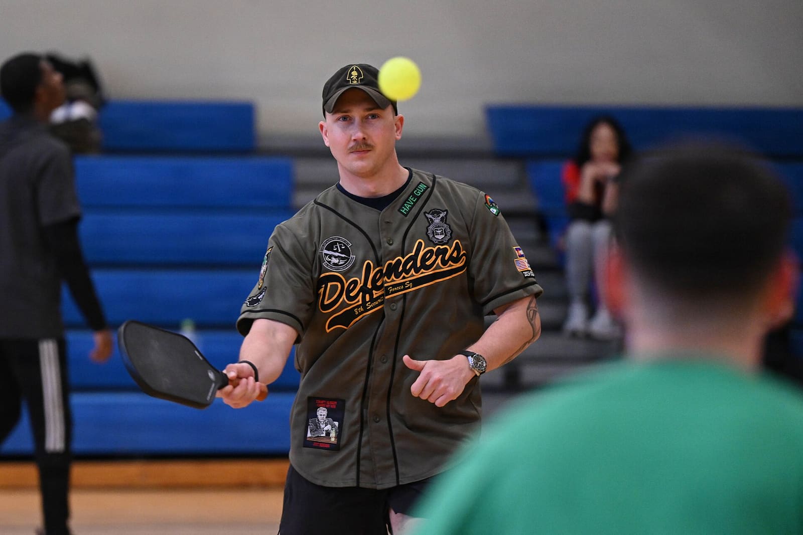 A player tosses the ball up for an underhand serve on an indoor pickleball court.